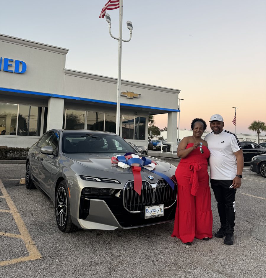 A client couple standing next to their new car at a dealership